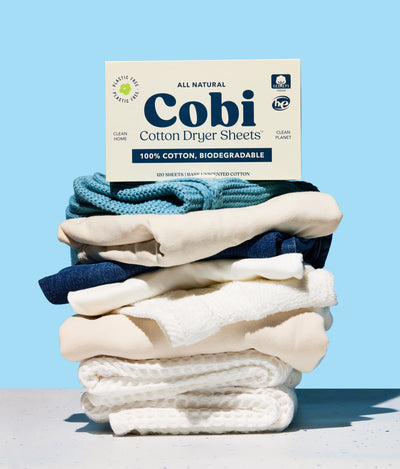 cobi dryer sheet box, unscented, ontop of folded laundry, blue background.
